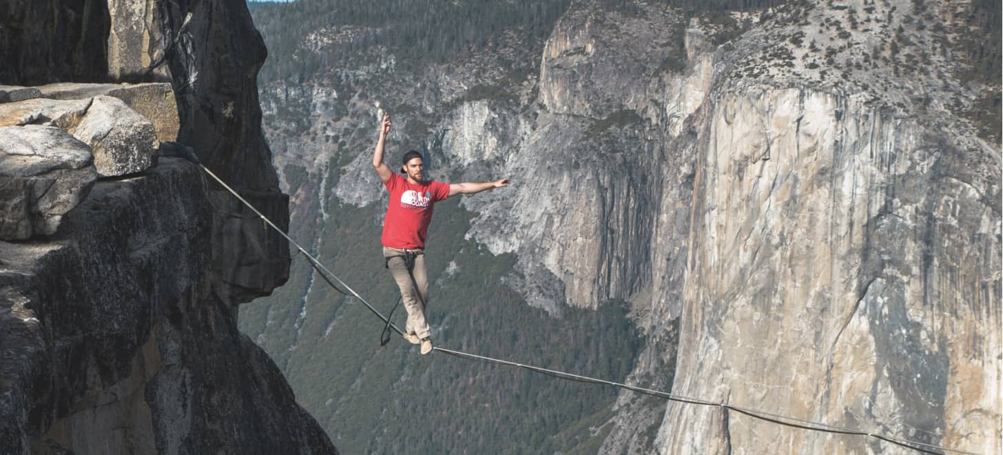 A young man walks a tightrope between the tops of two mountains