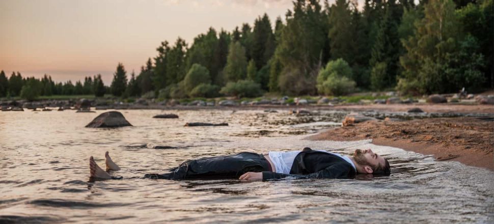 A young man cools off by lying down at the water's edge