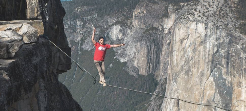 A young man walks a tightrope between the tops of two mountains