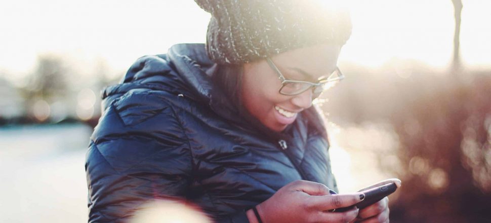 smiling woman wearing black coat using smartphone